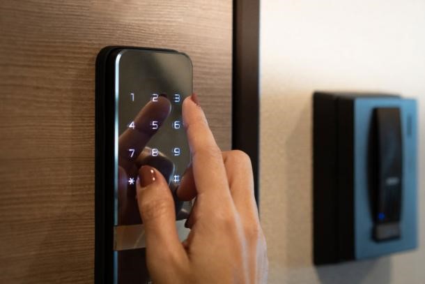 Imagine in prim plan a degetului unei femei care introduce codul parolei pe o tastatura digitală inteligentă cu ecran tactil pentru a debloca usa unei o camere de hotel.